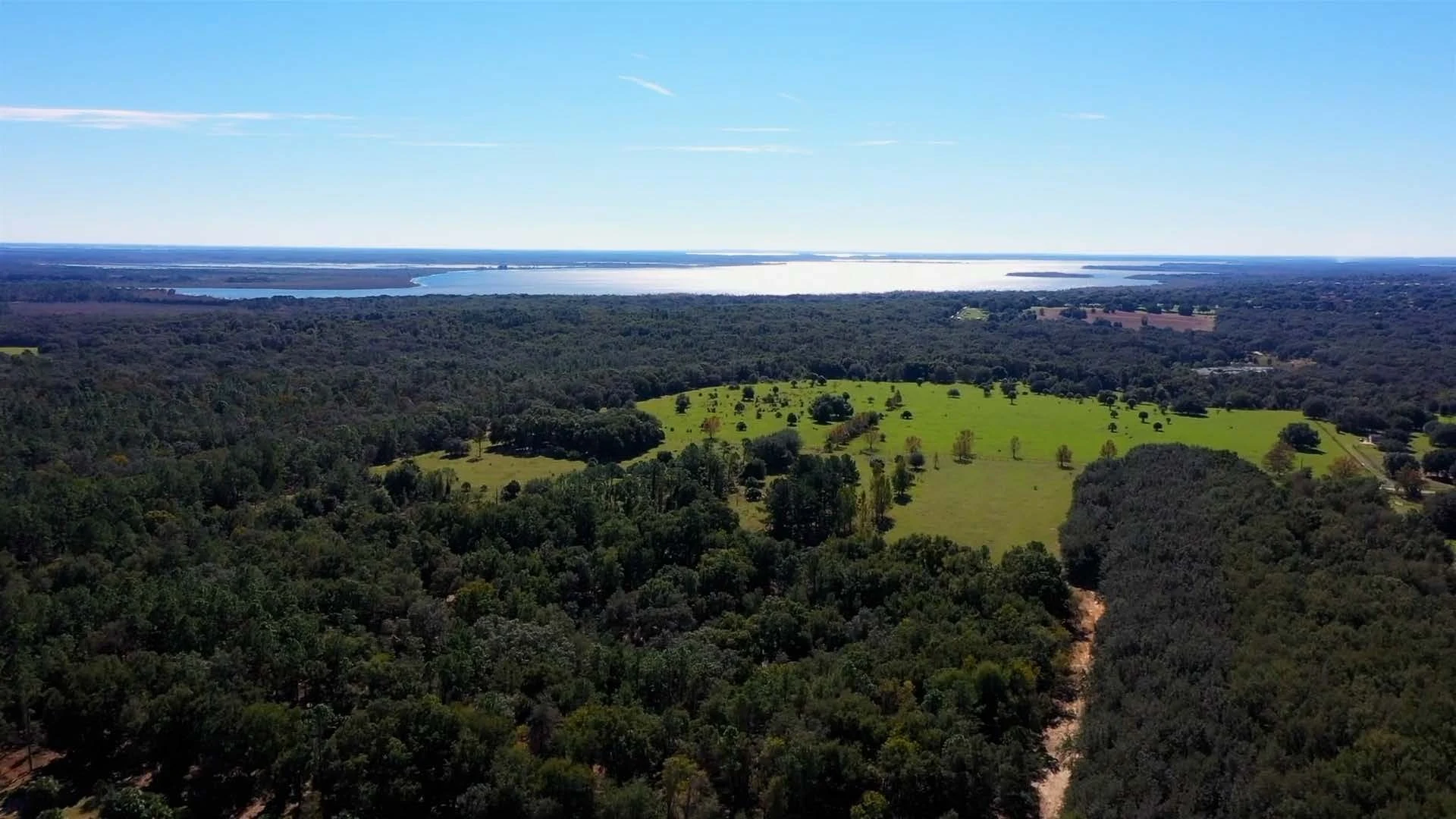 Aerial view of open pastures and wooded land with water along the horizon